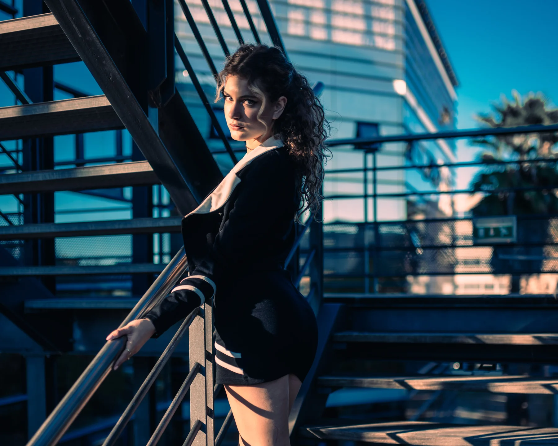 Mode Montpellier, femme en veste noire sur escalier métallique urbain, ambiance nocturne contrastée.