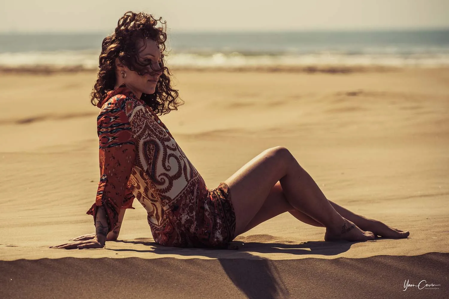 Femme en robe patterned lors d'une séance plage Camargue, lumière dorée, pose élégante sur le sable